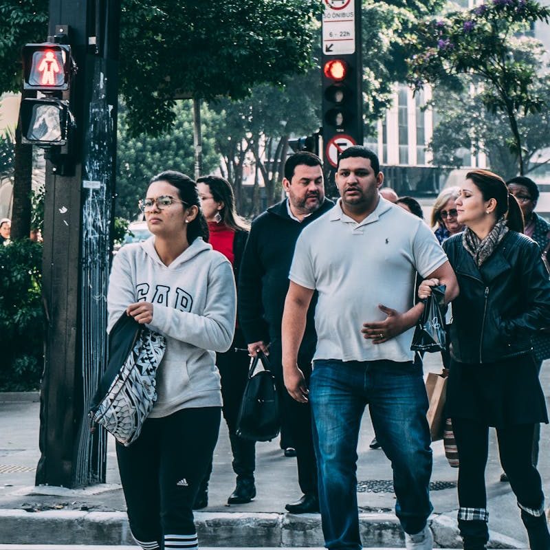 A diverse group of people crossing a street in a bustling city setting with skyscrapers.